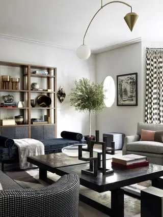 Sala de estar moderna com impressionante plafon geométrico, mesa de centro preta, duas poltronas e sofá azul, planta de casa, estante de madeira, janela redonda, obras de arte na parede.