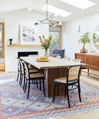 Une idée de salle à manger avec des murs blancs, une table et des chaises de style scandinave, un tapis bleu et rouge et un lustre spoutnik noir