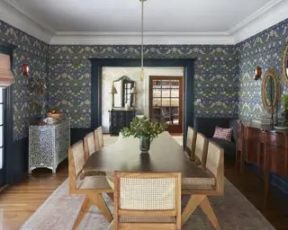 Une idée de salle à manger avec du papier peint bleu imprimé William Morris, un grand buffet en bois foncé et une table à manger en bois clair avec des chaises en rotin
