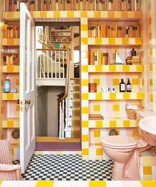 Salle de bains carrelée colorée, rose et jaune, étagères de niche présentant des ornements et des ornements décoratifs, toilettes roses, sol à carreaux