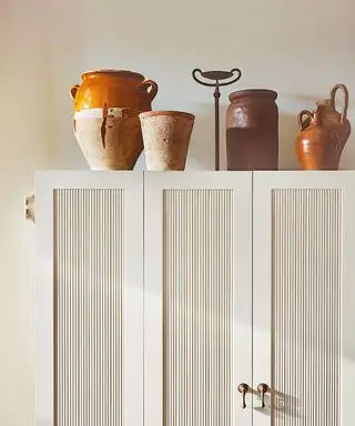 Grande armoire blanche avec des rideaux de fenêtre, décorée d'ornements et de céramiques posées sur le dessus