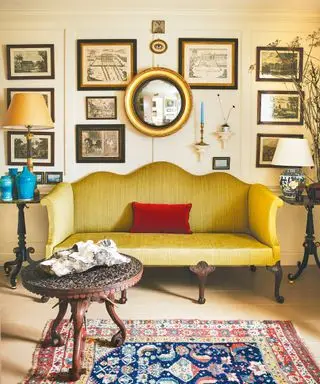 Salon de style ancien et vintage avec soda festonné vert, murs lambrissés blancs décorés d'œuvres d'art, table marron, tapis à motifs