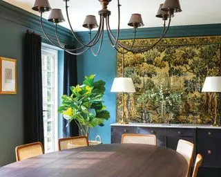 Salle à manger bleue avec tapisserie ancienne, table à manger en bois sombre, vase de fleurs, chandelier
