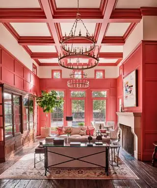 Grand espace de vie avec plafond à double hauteur, murs et plafond peints en rouge et rose, coin salon autour de la cheminée
