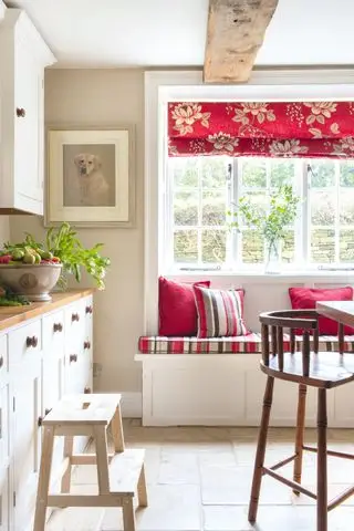 목재 조리대와 캐비닛이 있는 흰색 주방, 빨간색 블라인드가 있는 창가 좌석