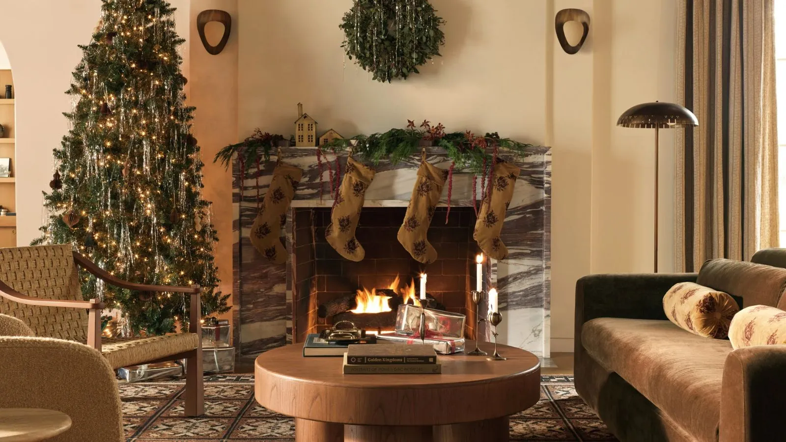lulu a georgia vánoční kampaň 2025 záběry náladového teplého obývacího pokoje s osvětleným mramorovým krbem zdobeným girlandou sametové punčochy sametová pohovka konferenční stolek zelená křesla a vánoční stromeček' loading='lazy' title=