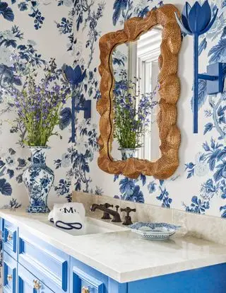 salle de bains avec papier peint bleu et blanc, miroir doré et vanité bleue