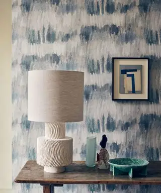 papier peint bleu mer pictural avec console en bois, lampe de table sculpturale et récipients
