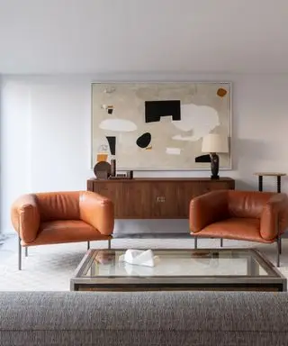 Warme vs. kühle Farben, modernes Wohnzimmer mit Retro-Sideboard und hellbraunen Ledersesseln, moderne Kunstwerke, großer Couchtisch mit Glasplatte, weiße Wände