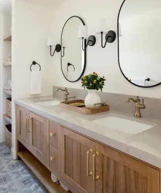 목재 캐비닛, 대리석 카운터, 금색 하드웨어 및 검정색 금속 액센트를 갖춘 캘리포니아 캐주얼 스타일의 욕실