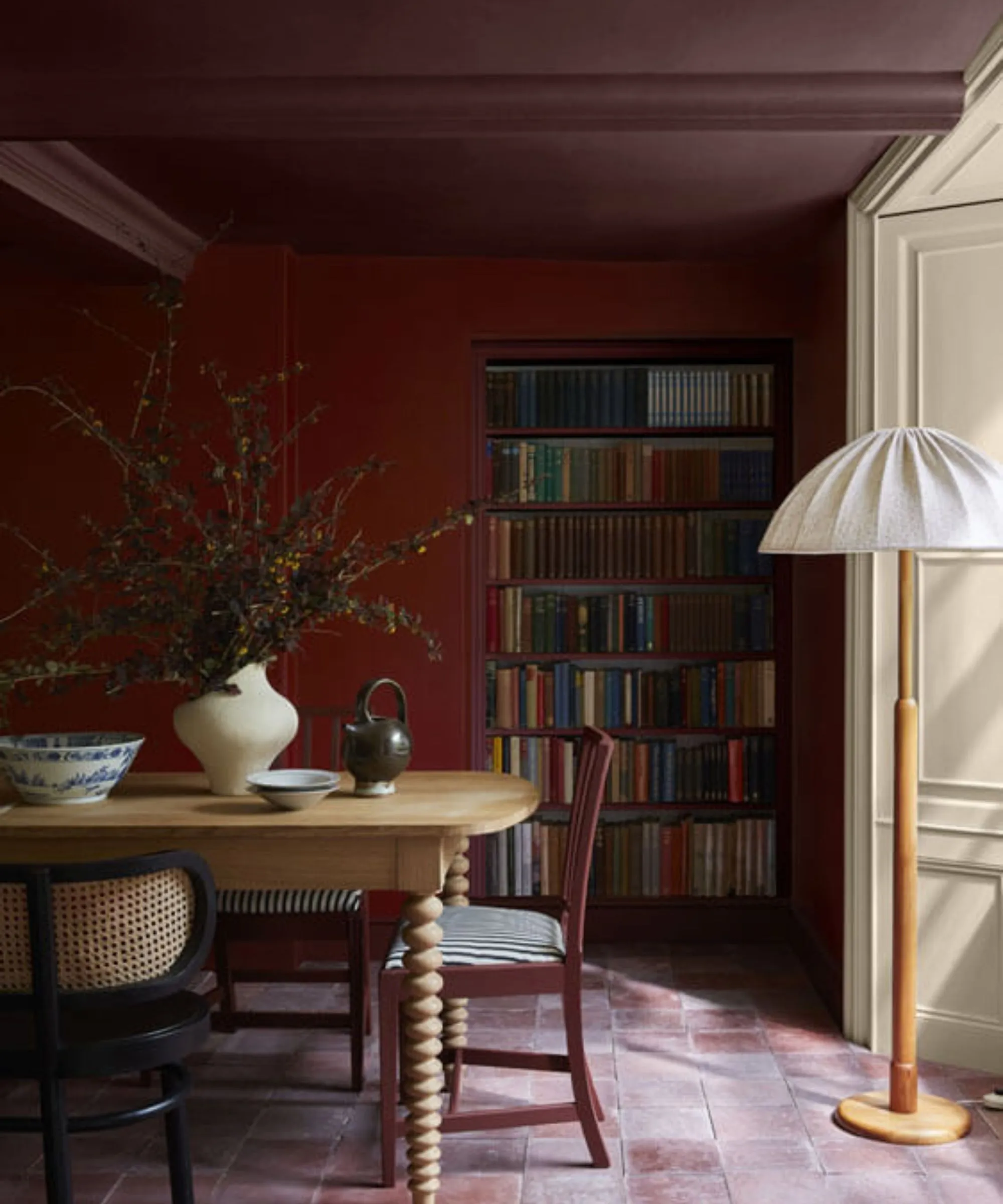 Farebná červená jedáleň s dreveným jedálenským stolom a zdobená vázou s jesenným lístím a drevenou lampou s bielym tienidlom' loading='lazy' title=