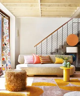 Lys, moderne stue med buet kremsofa, gult sidebord, fargerikt teppe og puter