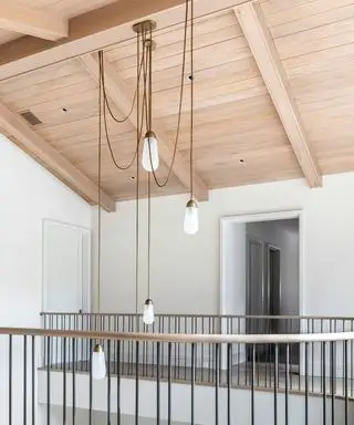 Palier avec plafond lambrissé en bois clair, murs peints en blanc, rampes d'escalier noires, suspensions d'ampoules sur fil