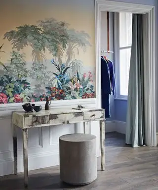 Chambre avec papier peint motif jungle, coiffeuse et assise pouf arrondie, porte donnant sur dressing, rideau séparant les espaces