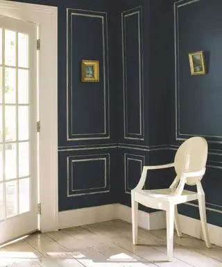 Couloir peint en bleu marine, effet lambris peint en or, deux cadres dorés aux murs, chaise blanche et parquet clair