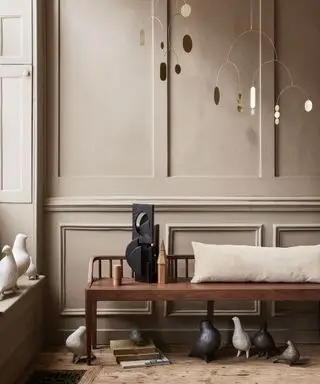 Banc en bois avec coussin beige devant des panneaux en bois peints en marron, mobiles décoratifs suspendus en métal, ornements d'oiseaux dispersés, parquet en bois foncé