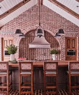 Salle à manger traditionnelle avec de belles briques sur les murs et le sol, grand îlot de cuisine en bois avec sièges, plafond voûté avec poutres en bois et boiseries blanches