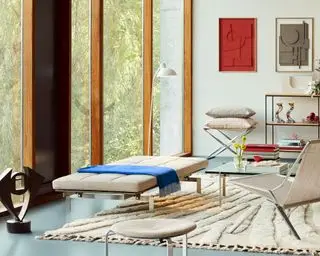 현대적인 거실 환경, 침대 겸용 소파, 안락의자, 유리 커피 테이블, 바닥에서 천장까지 이어지는 유리창, 선반 및 예술 작품을 배경으로 한 프리츠 한센 PK 컬렉션