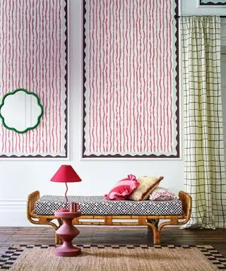 나무 프레임이 있는 작은 데이베드, 천을 씌운 좌석, 뒤쪽 벽에 걸린 두 개의 큰 예술 작품, 녹색 부채꼴 거울, 어두운 나무 바닥, 곡선형 사이드 테이블 및 그에 어울리는 테이블 램프