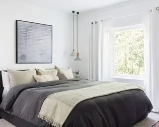 Chambre principale apaisante avec murs et rideaux peints en blanc, grand lit rembourré noir avec literie et coussins gris, œuvres d'art au-dessus du lit, pendentifs suspendus en béton