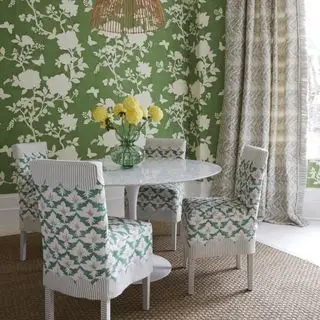 salle à manger avec papier peint à fleurs vert, table ronde blanche, chaises blanches en tissu et rideaux imprimés neutres