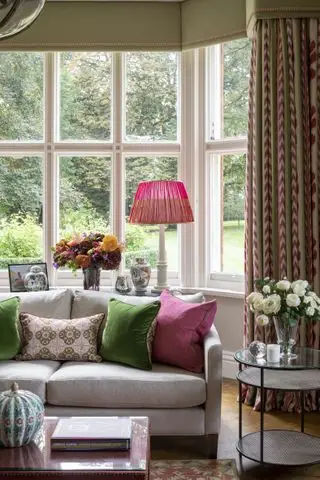 salon avec rideaux verts et rouges, baie vitrée, canapé gris, coussins lumineux, parquet