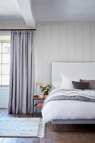 Chambre de style traditionnel avec grand lit, murs peints en vert, lustre à abat-jour, tapis noir et crème, commode noire avec miroir arrondi doré au-dessus, rideaux imprimés tropicaux