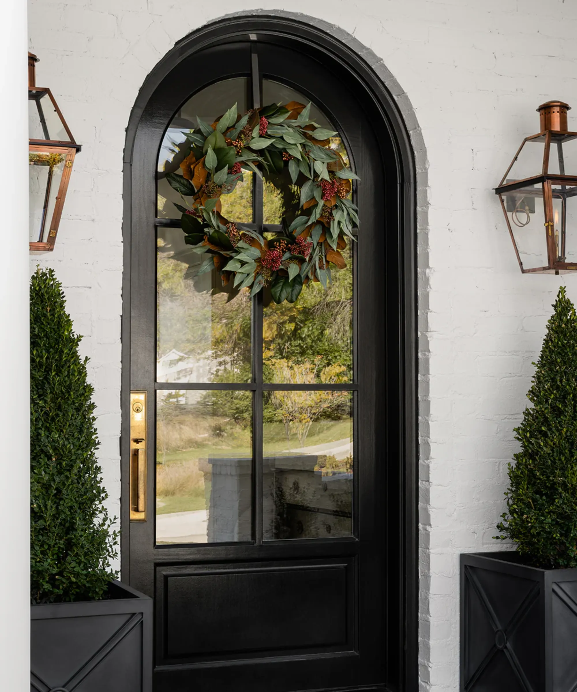czarne drzwi wejściowe, na których wisi wianek ze sztucznego eukaliptusa' loading='lazy' title=