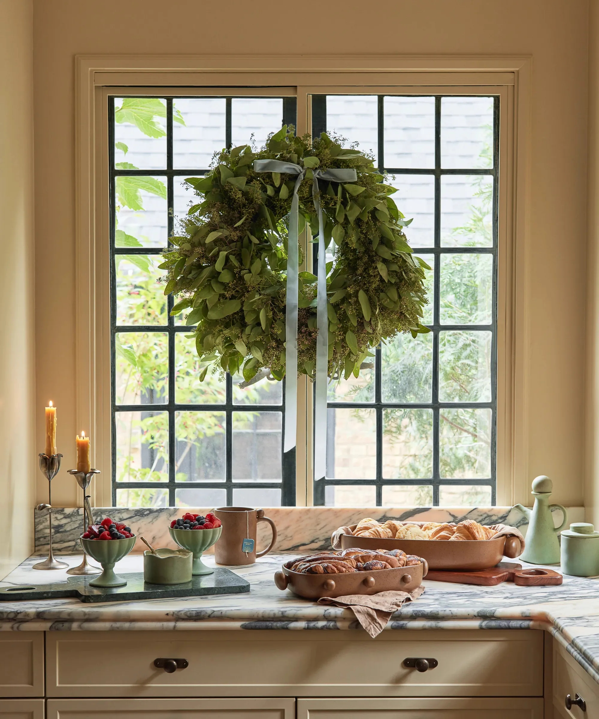 kuchnia z jedzeniem na blacie i ozdobnym wiankiem zwisającym z okna z niebieską kokardką' loading='lazy' title=