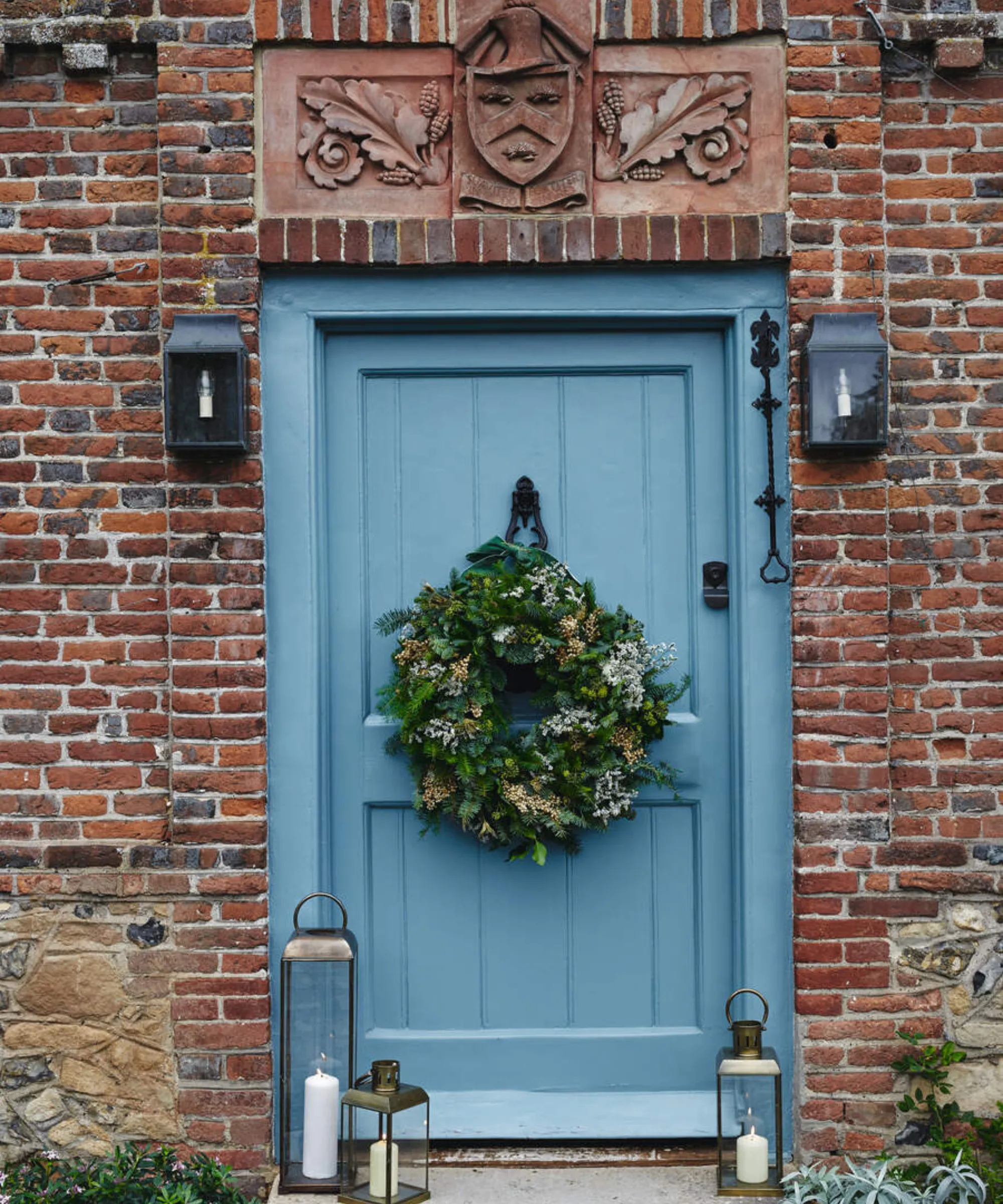 ceglany dom z niebieskimi drzwiami wejściowymi i wiszącym na nich wieńcem' loading='lazy' title=