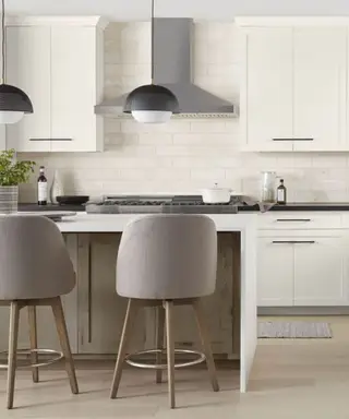Kuchyně natřená na bílo s ostrůvkem a šedými barovými židlemi.