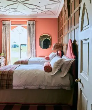 트윈 침대, 목재 패널 벽, 밝은 오렌지색 벽 및 천장 트레이서리를 갖춘 침실 출입구를 통해 전망을 감상하실 수 있습니다.