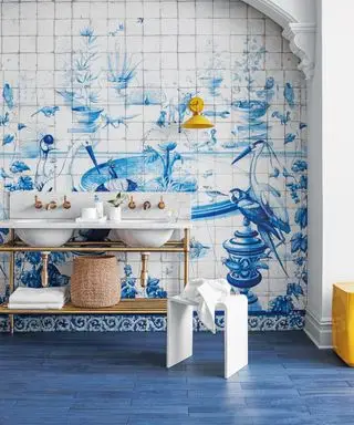Baño azul con mural de azulejos, piso azul, detalles en amarillo, lavabo doble en blanco y metal