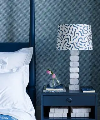 Dormitorio azul y blanco con cama azul con cuatro postes y mesita de noche, papel tapiz estampado y pantalla estampada