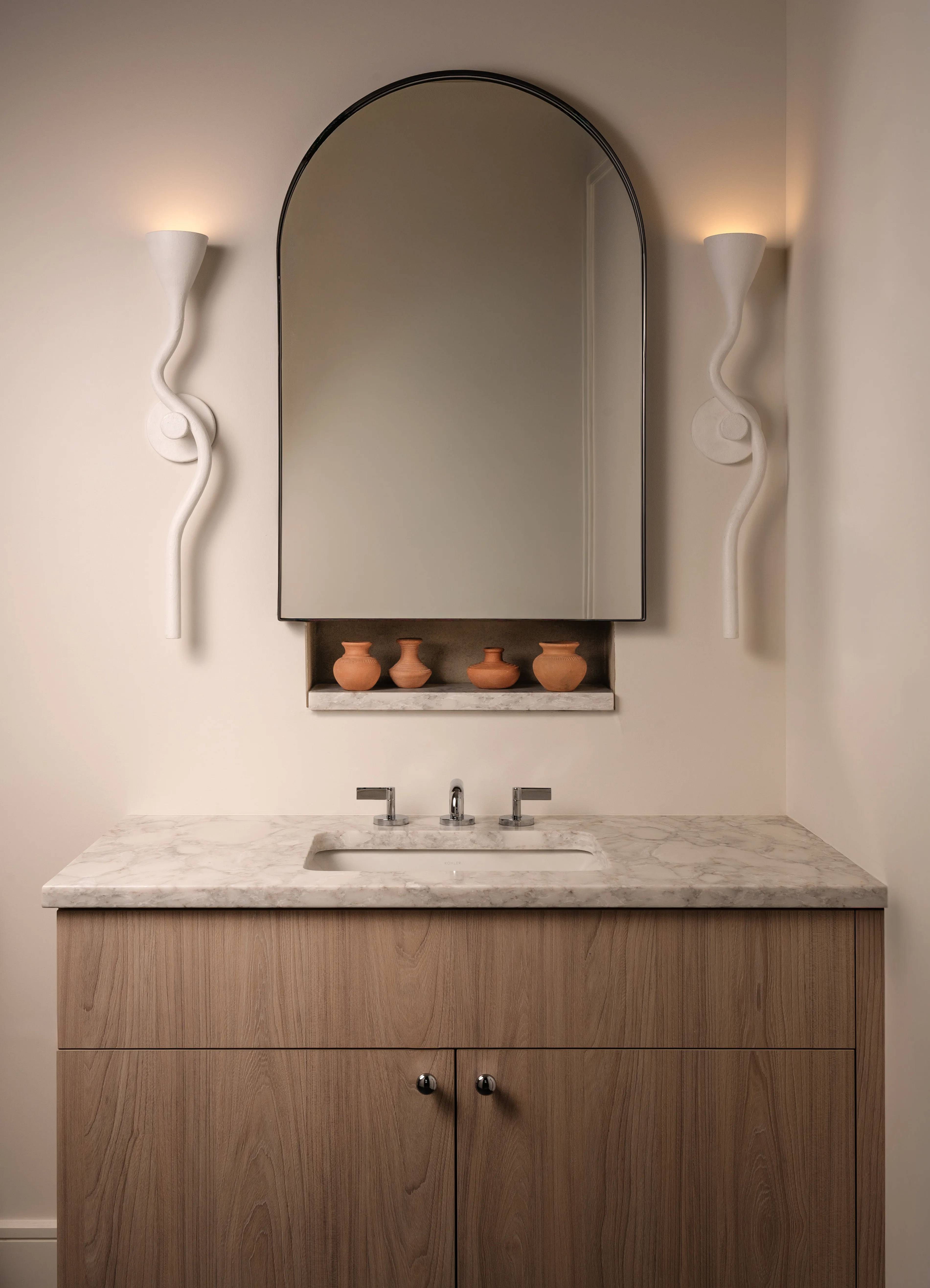 アーチ型の鏡と白いライトが両側にあるニュートラルな洗面化粧台エリアと、大理石のトップを備えた木製の洗面化粧台' loading='lazy' title=