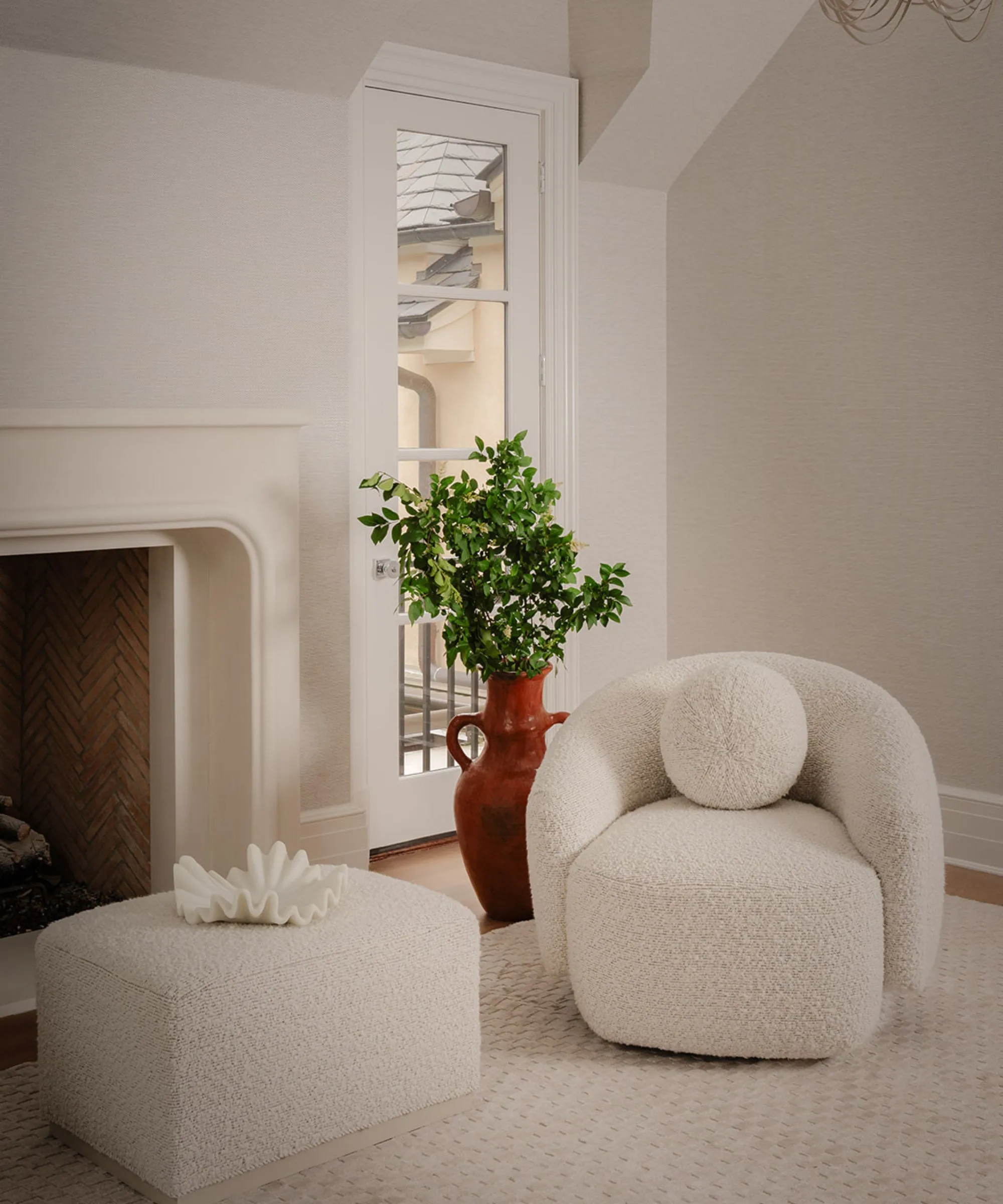 レンガ造りのインテリアの暖炉、ブークレ肘掛け椅子、お揃いのプーフ、緑がいっぱいの大きな花瓶を備えたクリーム色のリビング ルーム' loading='lazy' title=