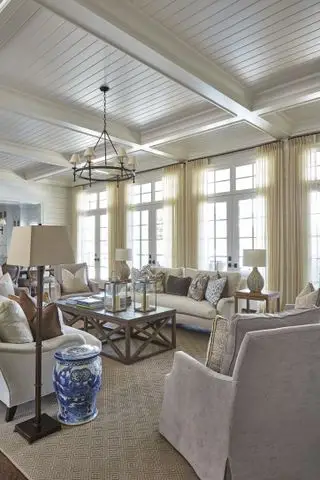 Salón con sillones y sofás, cortinas hasta el suelo y paleta neutra.