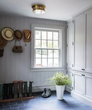 Un vestiaire simple avec des bottes en caoutchouc posées sur le sol, des chapeaux rangés sur des patères et une grande fenêtre