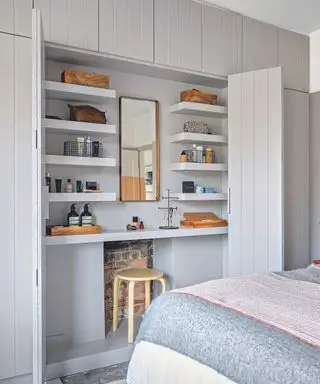 Une chambre avec de grandes portes de placard ouvertes sur une coiffeuse à l'intérieur, boiseries peintes en gris pâle. Placards et rangements intégrés au mur. Chambre principale