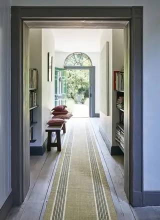 entrée avec plancher en bois, tapis à rayures, bibliothèques de chaque côté, banc avec coussins, porte d'entrée ouverte