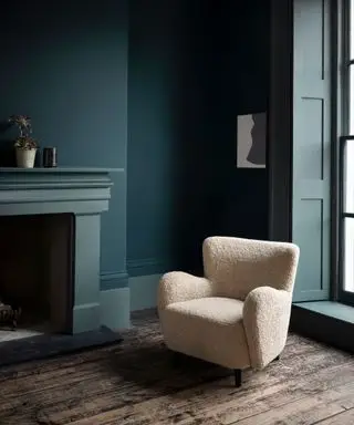 Grün gestrichenes Wohnzimmer mit cremefarbenem Loungesessel und Kamin