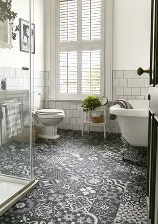 salle de bain blanche avec baignoire sur roulettes, volets, sol gris, noir et blanc à motifs en vinyle