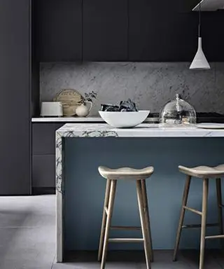 Szara kuchnia z blokami kolorystycznymi w kolorze jasnoniebieskim, marmurkowy bar śniadaniowy i stołki barowe.