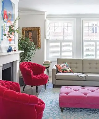 Una sala de estar blanca con impactantes muebles de color rosa, una alfombra azul con motivos geométricos y arte moderno.