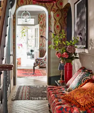 Fargerik og levende rød gang med lavmønstret divan og mønstret tapet, tregulv