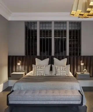 Moderne, minimalistisk soverom med gråmalte vegger, forlenget svart trukket hodegjerde, grått sengetøy, grå divan ved fotenden av sengen, mørkt tregulv, pendellampe i gull