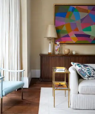 Obývací pokoj se zlatými tapetovanými stěnami, propracovanou římsou, dřevěnou podlahou a bílým kobercem.