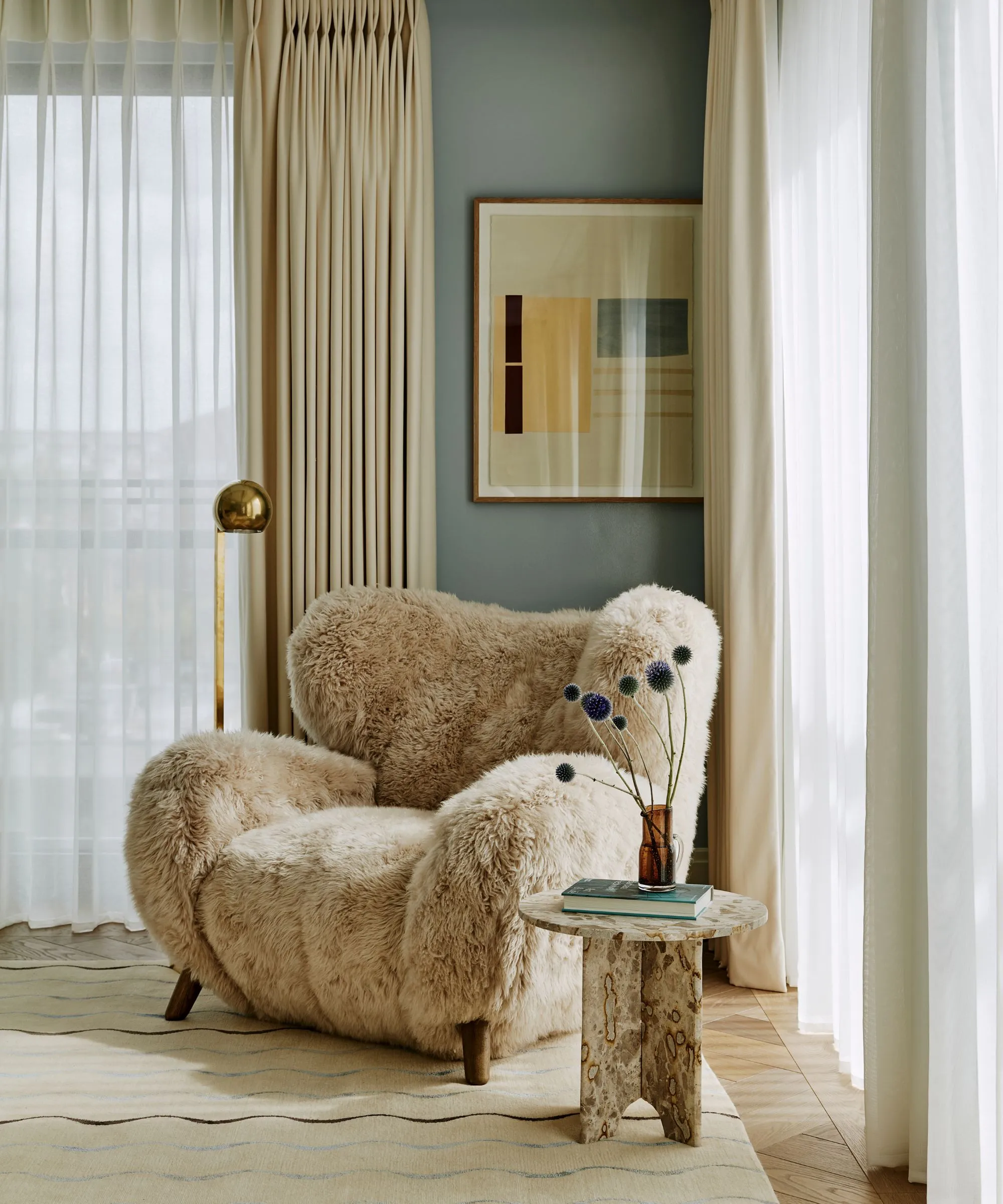 부드러운 파란색 아늑한 현대 침실 큰 창문이있는 중성 깔개가있는 중성 깔개가있는 중립 깔개 푹신한 양가죽 안락 의자가 꽃병과 바닥 램프가 달린 미니 대리석 테이블로 가득합니다.' loading='lazy' title=