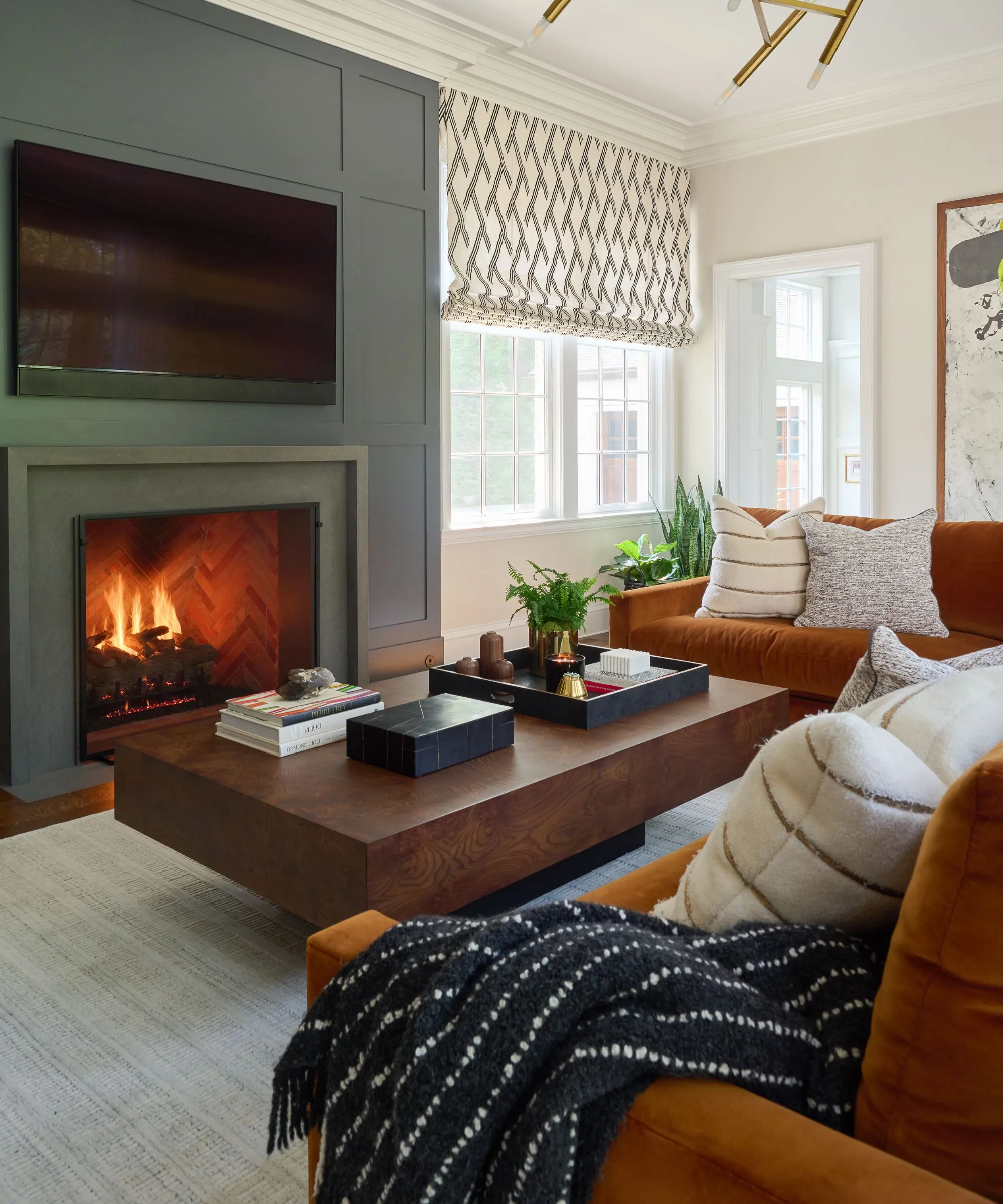 벽난로 패널이있는 녹색과 주황색 아늑한 현대 거실은 흙빛 녹색 불이 붙은 나무 커피 테이블과 큰 녹 주황색 벨벳 소파' loading='lazy' title=