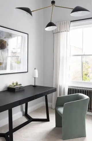bureau à domicile avec bureau noir, fauteuil vert, lampe de table, suspension rétro, radiateur, murs gris, œuvres d'art, rideaux, tapis